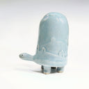 Ceramic turtle figurine with a light blue glaze and a subtle design of hills and houses on a white background