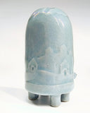 Ceramic turtle figurine with a light blue glaze and a subtle design of hills and houses on a white background