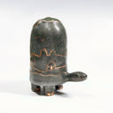 Dark grayish green ceramic turtle sculpture, with a very tall shell and a bronze line art illustration of hills and houses around its shell.