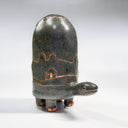 Dark grayish green ceramic turtle sculpture, with a very tall shell and a bronze line art illustration of hills and houses around its shell.