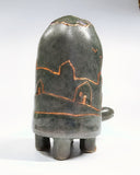 Dark grayish green ceramic turtle sculpture, with a very tall shell and a bronze line art illustration of hills and houses around its shell.