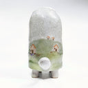 Ceramic sculpture of a turtle with a very tall shell, which has a landscape design on it of a grassy hill and small houses.