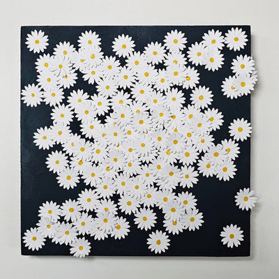 Black wooden panel covered in small white flowers cut out of paper and adhered, coating most of the panel's surface. Each flower has a small yellow dot as the center.