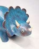 Blue textured ceramic sculpture of a stegosaurus with small horns and a curled tail.