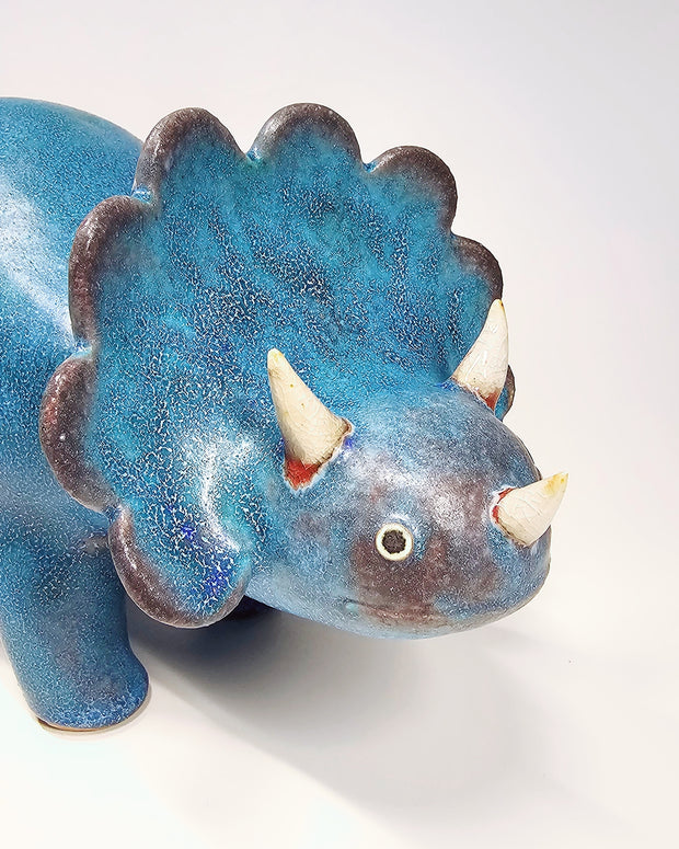 Blue textured ceramic sculpture of a stegosaurus with small horns and a curled tail.