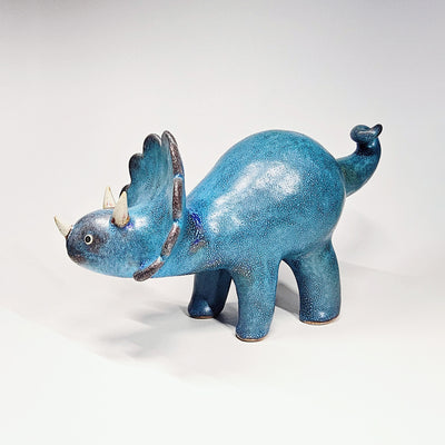 Blue textured ceramic sculpture of a stegosaurus with small horns and a curled tail.