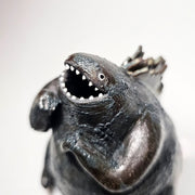 Ceramic Godzilla figure with a surface finishing akin to cooled magma, black with a subtle sheen. It has a very small, smooth head and a large plump body and back spikes.