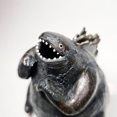Ceramic Godzilla figure with a surface finishing akin to cooled magma, black with a subtle sheen. It has a very small, smooth head and a large plump body and back spikes.