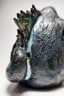 Ceramic Godzilla figure with a surface finishing akin to cooled magma, black with a subtle sheen. It has a very small, smooth head and a large plump body and back spikes.