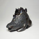 Ceramic Godzilla figure with a surface finishing akin to cooled magma, black with a subtle sheen. It has a very small, smooth head and a large plump body and back spikes. It lays on the ground
