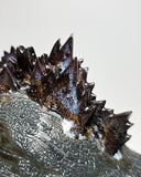 Ceramic Godzilla figure with a surface finishing akin to cooled magma, black with a subtle sheen. It has a very small, smooth head and a large plump body and back spikes. It lays on the ground