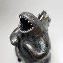Ceramic Godzilla figure with a surface finishing akin to cooled magma, black with a subtle sheen. It has a very small, smooth head and a large plump body and back spikes.