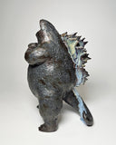 Ceramic Godzilla figure with a surface finishing akin to cooled magma, black with a subtle sheen. It has a very small, smooth head and a large plump body and back spikes.