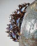 Close-up of a ceramic sculpture with textured surface and spikes on a light gray background
