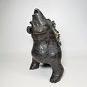 Ceramic Godzilla figure with a surface finishing akin to cooled magma, black with a subtle sheen. It has a very small, smooth head and a large plump body and back spikes. It stands and throws its head back, as if laughing.