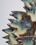 Close-up of a ceramic sculpture with textured surface and blue and brown glaze on a light gray background