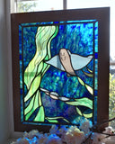Stained glass artwork of a bat ray with a blue and green background, framed in front of a window.