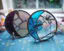 2 Circular stained glass artworks, one with flowers coming off of it and the other in the shape of a crescent moon.