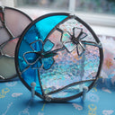 Circular stained glass artwork with flowers coming off of it.