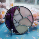Circular stained glass artwork that looks like a crescent moon, purple and white.