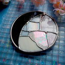 Circular stained glass artwork that looks like a crescent moon, purple and white.