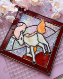 Stained glass artwork of a white horse with a mane and tail made out of flames, on a pink background with flowers