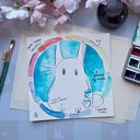 Watercolor sketch of a chibi Totoro within a colorful circle.