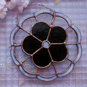 Stained glass wall hanging art of a flower, with 5 petals and a circular center. The flower is a dark, iridescent coloring and is outlined in clear, wavy glass and a blue outline.