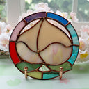Stained glass artwork of a peach, upside down so the leaves are at the bottom. It is encased in a rainbow colored stained glass circle border.