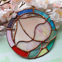 Stained glass artwork of a peach, upside down so the leaves are at the bottom. It is encased in a rainbow colored stained glass circle border.