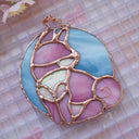 Stained glass hanging art of a Shiba Inu dog, silhouetted by its white markings and pink coloring for its fur. Background is a blue glass circle.