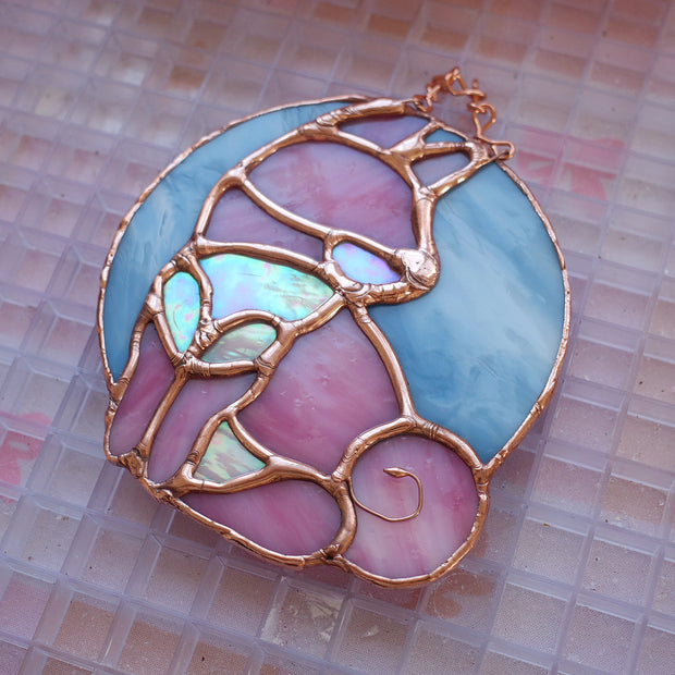 Stained glass hanging art of a Shiba Inu dog, silhouetted by its white markings and pink coloring for its fur. Background is a blue glass circle.