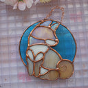 Stained glass hanging art of a Shiba Inu dog, silhouetted by its white markings and iridescent purplish green coloring for its fur. Background is a blue glass circle.