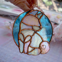 Stained glass hanging art of a Shiba Inu dog, silhouetted by its white markings and iridescent purplish green coloring for its fur. Background is a blue glass circle.