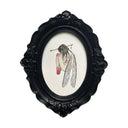 An ornate oval black frame containing a gothic-style illustration of a fairy, curled up with wings and a bow shot through her head, on a white background.