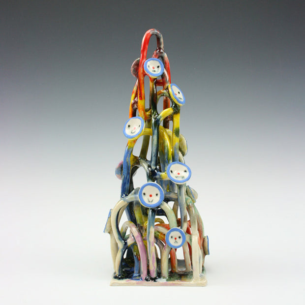Ceramic sculpture of many looping shapes, like a stretched out pile of yarn. it is multicolor and has simple smiley faces like buttons, with blue outlines and simple features.
