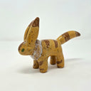 Small ceramic sculpture of a brown animal figure with very tall ears, a pointed tail and a white fur collar. It has darker brown striping and green eyes.