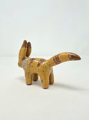 Small ceramic sculpture of a brown animal figure with very tall ears, a pointed tail and a white fur collar. It has darker brown striping and green eyes.