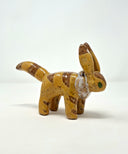 Small ceramic sculpture of a brown animal figure with very tall ears, a pointed tail and a white fur collar. It has darker brown striping and green eyes.