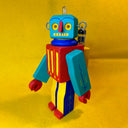 Colorful toy robot made out of wood, with moveable arms and wire attachments coming out of the side of its head and lights on its head and back.