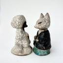 Pair of ceramic figurines of foxes, one wears a robe and the other wears more traditional Japanese clothing. They face one another. 