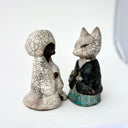 Pair of ceramic figurines of foxes, one wears a robe and the other wears more traditional Japanese clothing. They face one another. 