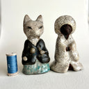 Pair of ceramic figurines of foxes, one wears a robe and the other wears more traditional Japanese clothing. They face one another. 