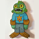 Colorful die cut sea creature character, with an open mouth showing many teeth and large green eyes. It stands on webbed feet and wears floatation devices around its arms.