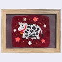 Felted artwork of a cow with flowers in a wooden frame on a red background