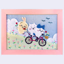 Framed artwork of three cartoon animals from Chiikawa, riding on a bicycle down a green hill with lots of flowers.