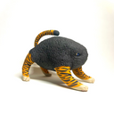 A small sculptural animal figure resembling a cat or tiger, with a dark charcoal textured body, orange-and-black striped legs and tail, and cream paws, photographed on a clean white studio background.