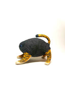 A small sculptural animal figure resembling a cat or tiger, with a dark charcoal textured body, orange-and-black striped legs and tail, and cream paws, photographed on a clean white studio background.