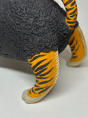 Close-up of a tiger-striped animal figurine showing bright orange paws and legs with black stripes, a dark gray textured body, and cream-colored feet on a plain light background.