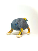 A small sculptural figurine of a four-legged creature with a dark charcoal-black textured body, bright orange and yellow striped legs, and blue eyes, photographed on a plain white studio background.